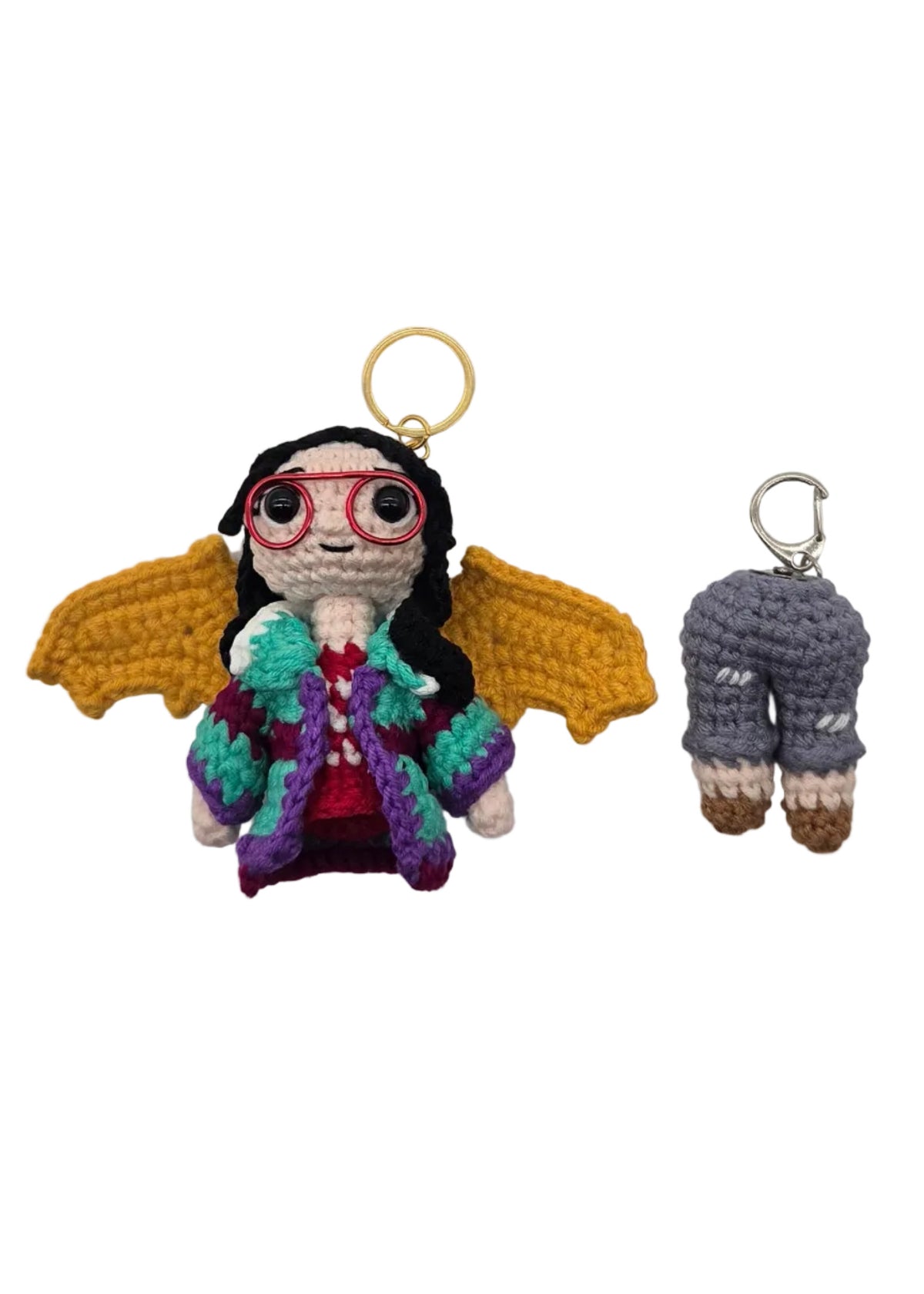 Two small crocheted keychains on a plain white background, one upper body half with a gold key ring and one lower body half with a silver key ring.