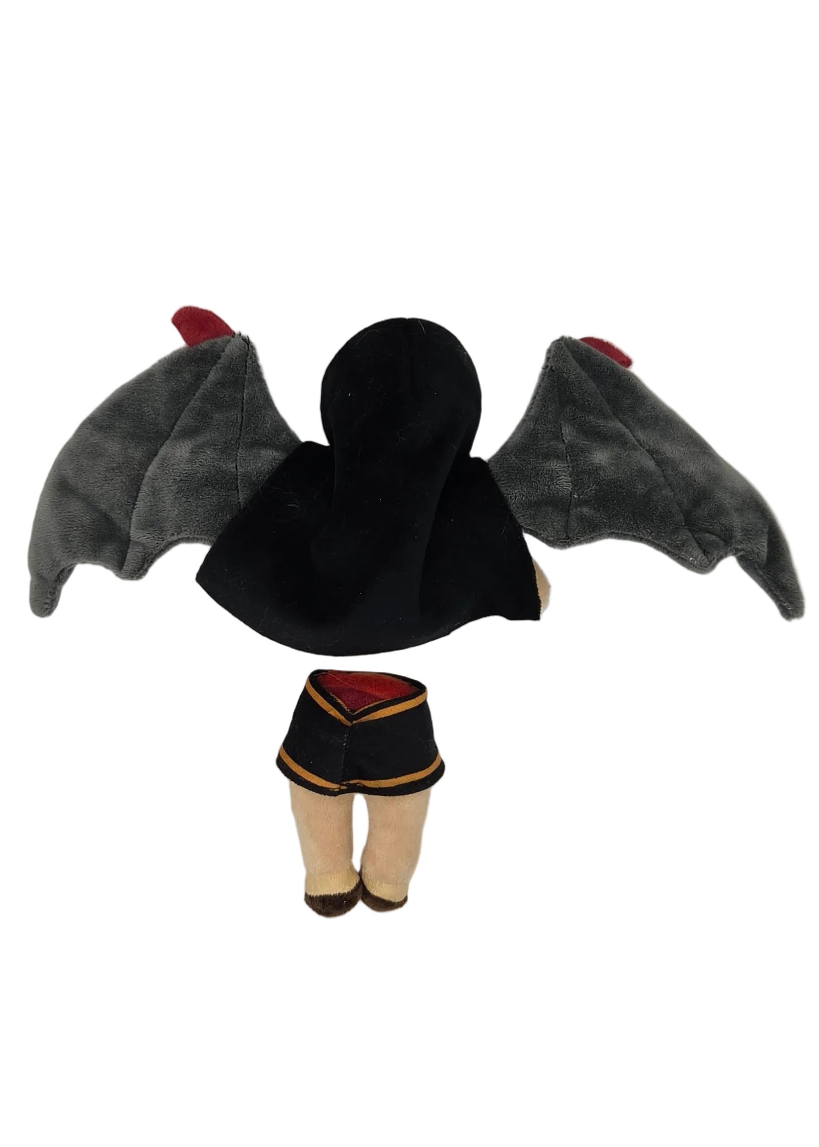 A small doll viewed from above, wearing a black skirt with gold trim and gray wings, against a plain light background.
