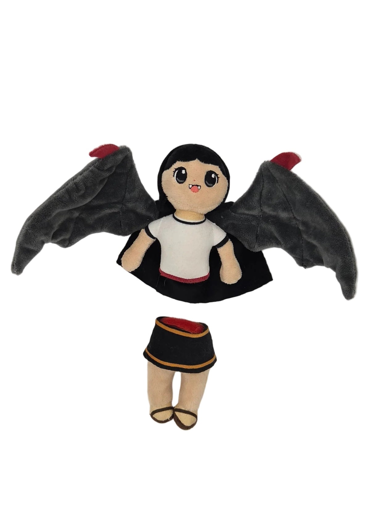 A small doll with black bat-like wings, a black dress, and a white top, photographed against a plain light background.