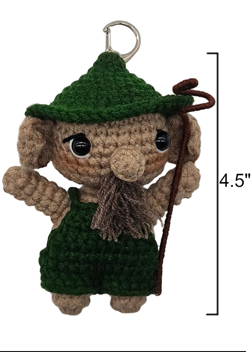 A handmade crocheted dwende with a green cap, brown beard, and green overalls, shown against a plain white background. A black measurement bracket on the right indicates a height of 4.5 inches.