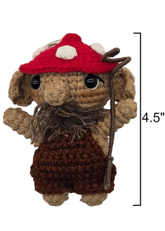 A handmade crocheted dwende with a red mushroom cap, brown beard, and brown overalls, shown against a plain white background. A black measurement bracket on the right indicates a height of 4.5 inches.