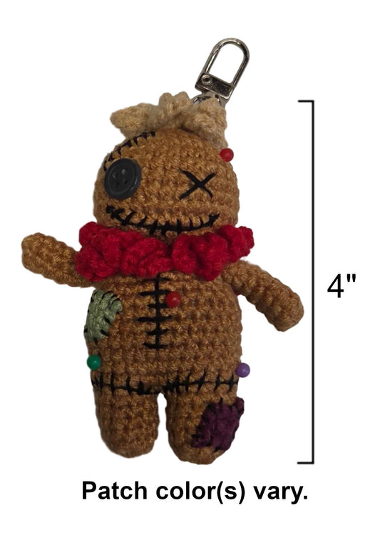 A crocheted voodoo doll keychain charm in brown yarn with a red scarf, black stitched details, and colorful embroidered patches, shown on a white background with a 4-inch height marker and text noting patch color variation.