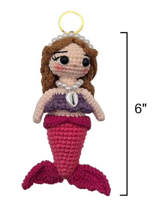 A crocheted sirena doll on a gold keychain, brown hair, a purple top, shell necklace, and pink tail, shown on a white background with a 6-inch height marker.
