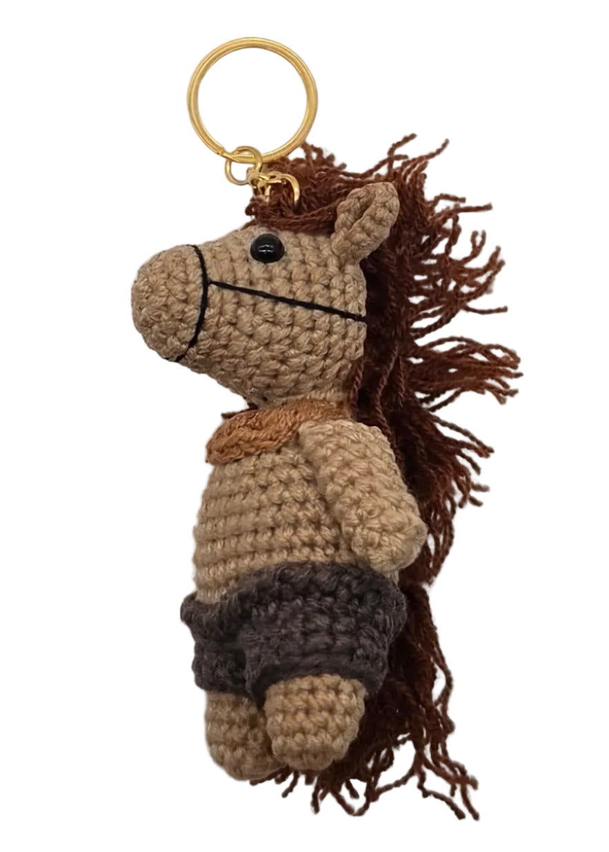 A small crocheted horse keychain with a yellow ring, placed on a white surface. 